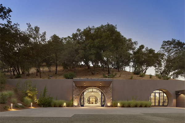 Modern building with arched entryways, set against a hillside with trees, under a clear evening sky.