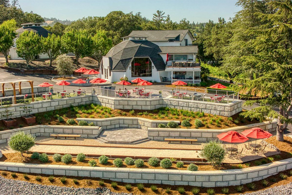 A terraced outdoor seating area with red umbrellas overlooking a building surrounded by trees.